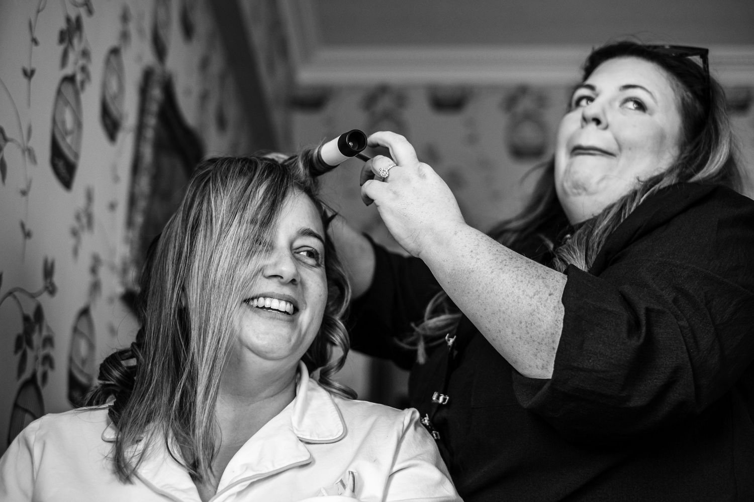 A joyful black and white moment during wedding preparations with hair styling.