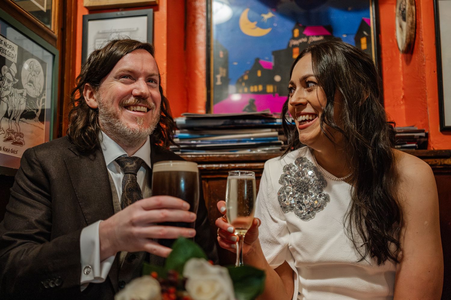 Wedding guests celebrate and socialize in a warmly lit pub with red walls.