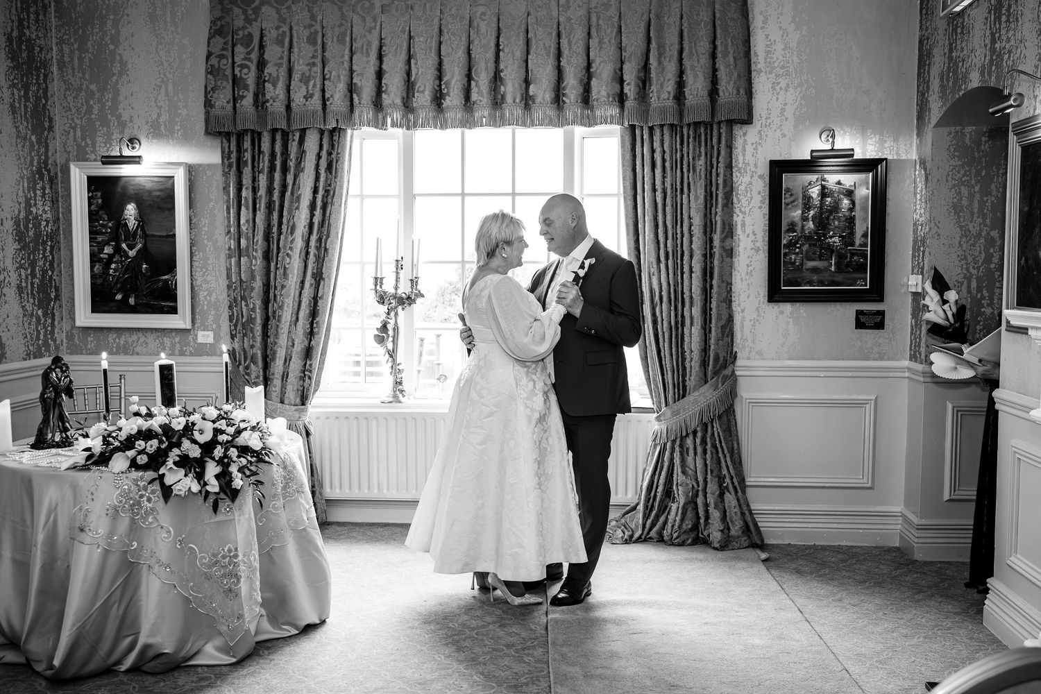 Black and white photo of bride and groom sharing first dance in elegant wedding venue.
