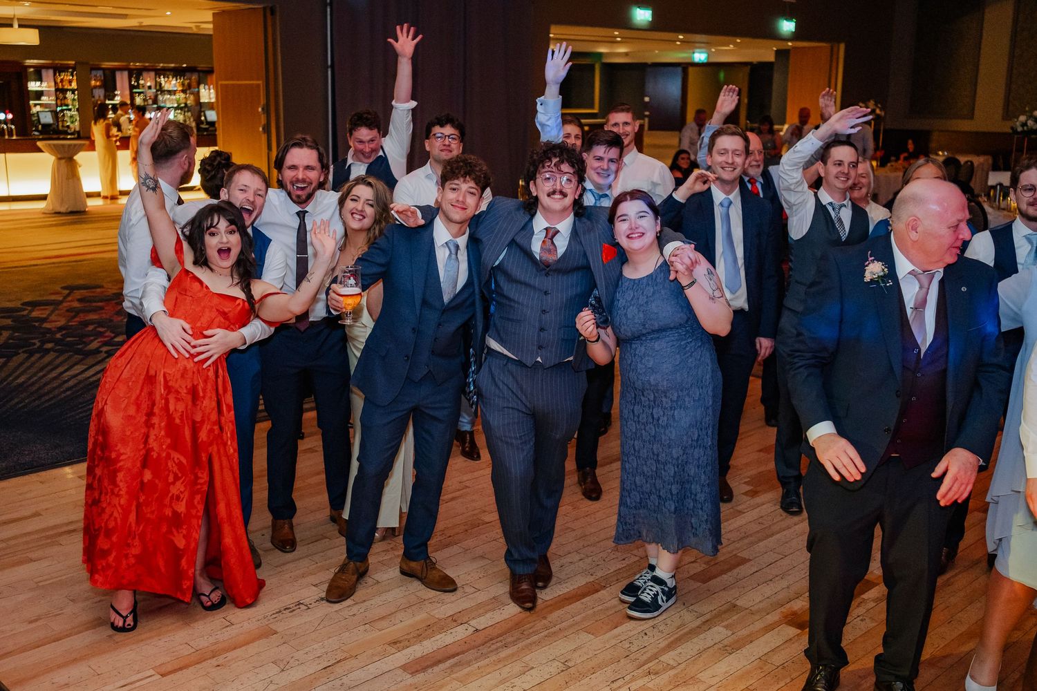 Wedding guests dance together in a ballroom during an evening reception celebration.