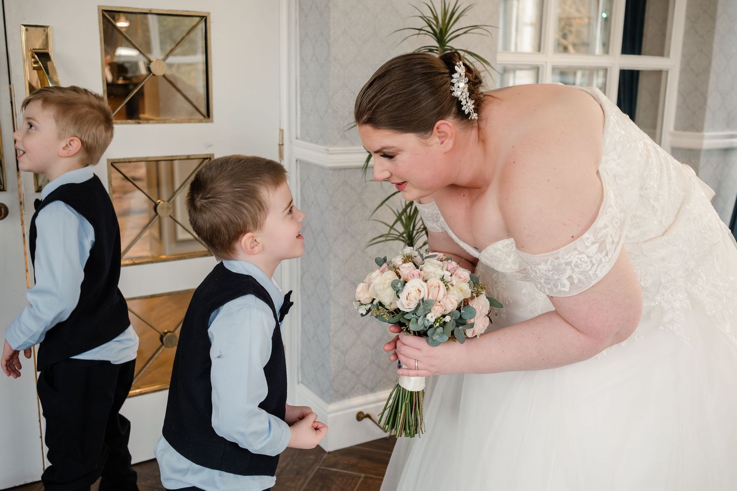Tender wedding moment with young children in formal attire indoors.