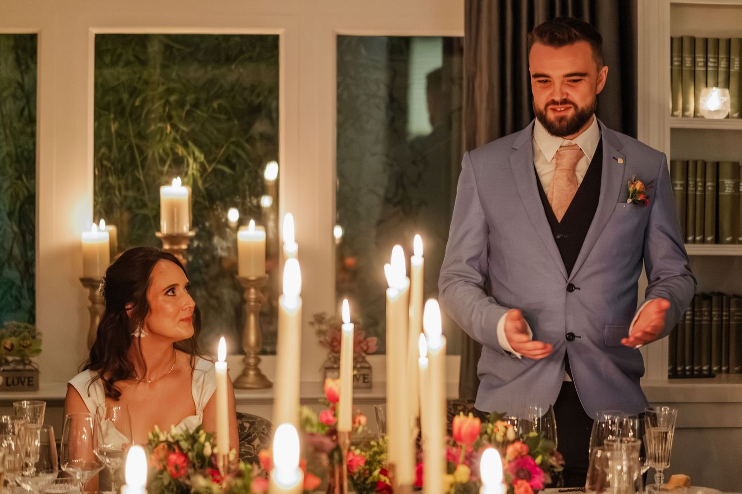 A candlelit wedding reception dinner table with floral centerpieces and elegant place settings.