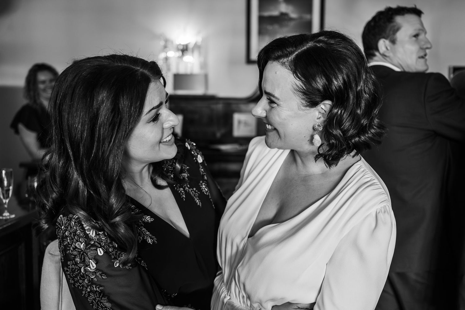 Two women share a joyful moment laughing together at a social gathering in this black and white photo.