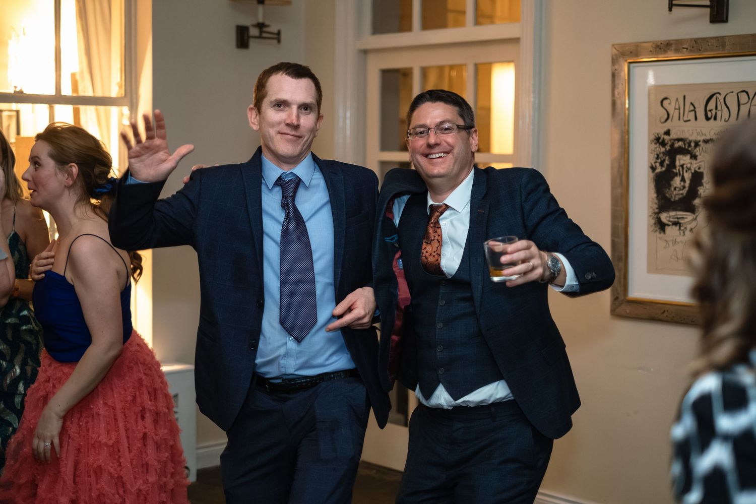 Two men in suits dancing and posing joyfully at a wedding reception party.