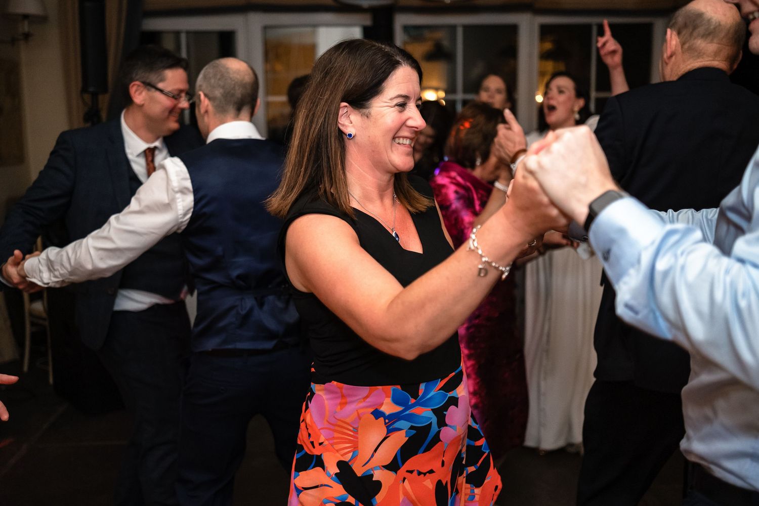 Woman in floral skirt smiling and dancing energetically at a wedding reception.