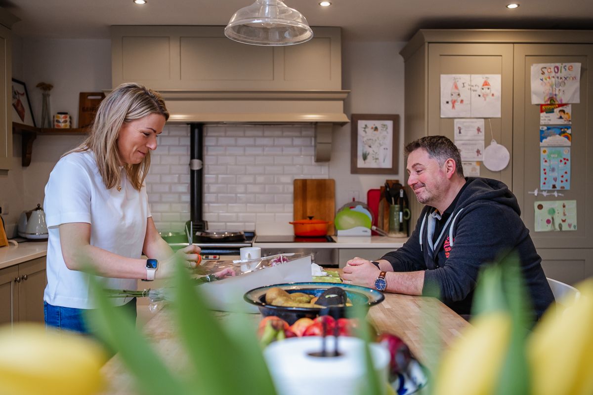 Two parents in a modern kitchen smiling and prepping food an flower arrangements