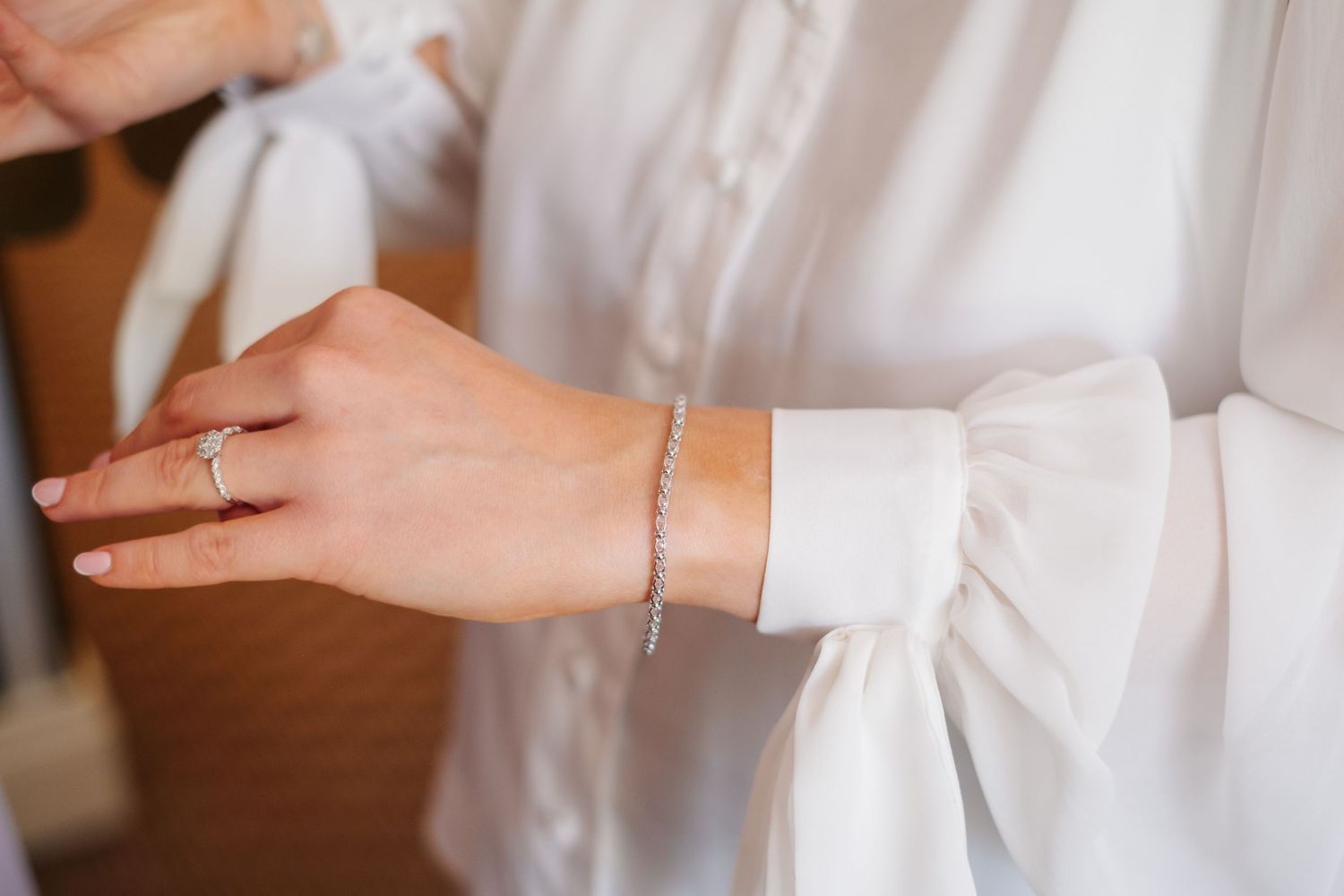 Cropped details of someone in an elegant white wedding dress adjusting lace buttons and fabric.
