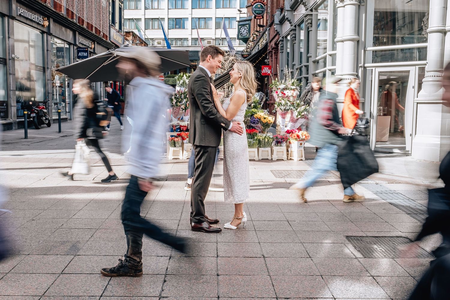 Couple stands still while people blur past in motion on busy city street.