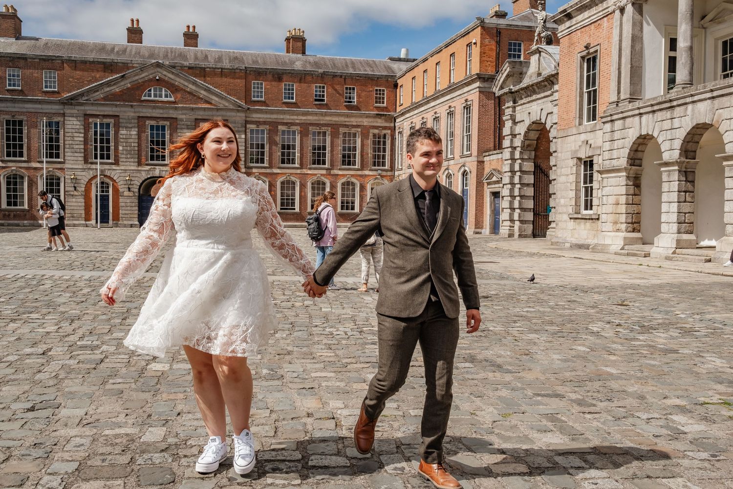 A couple in wedding attire dances together in a historic courtyard with Georgian architecture.