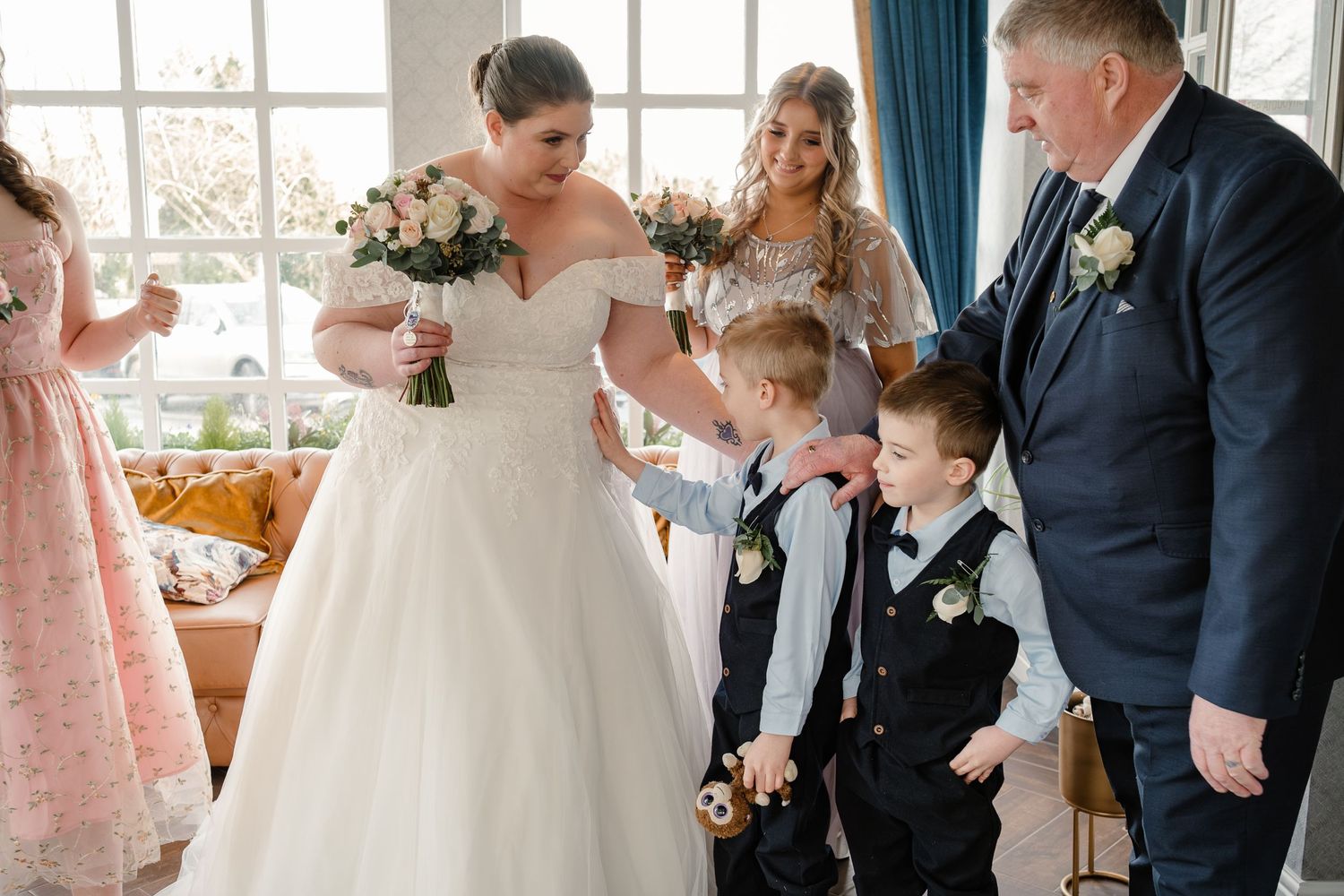 A wedding party gathers indoors with two young ring bearers and elegant bouquets.