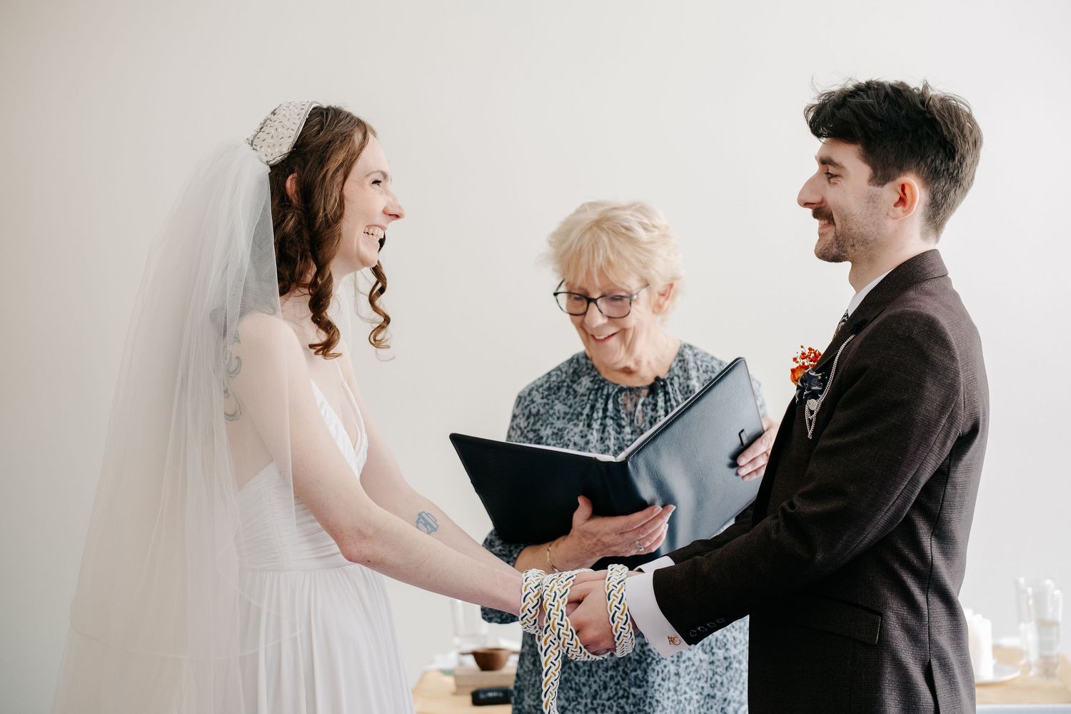 Wedding ceremony participants share joyful laughter during candid moments in a bright indoor setting.
