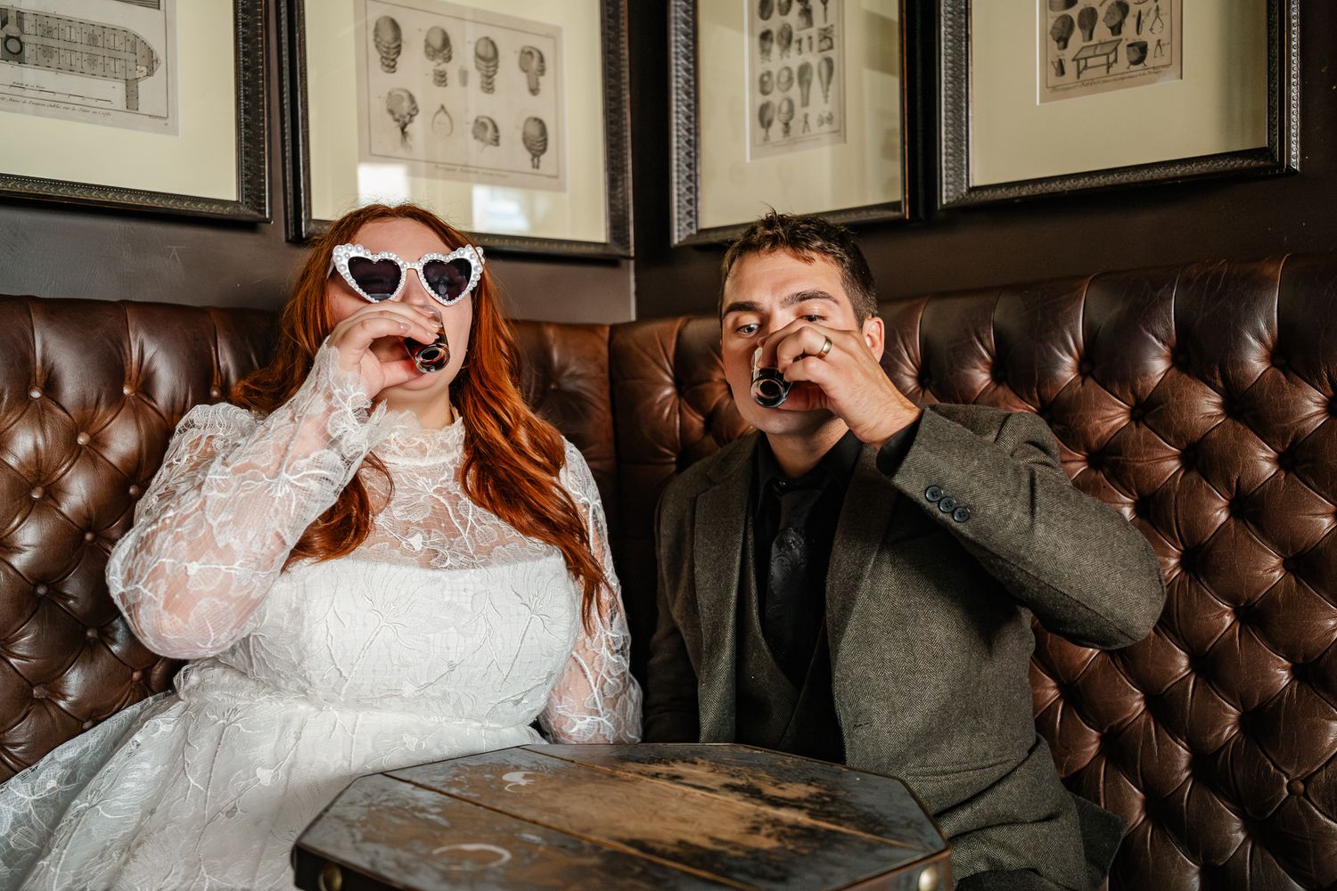 Interior of a vintage bar with leather seating and framed portraits on dark walls with a bride and groom having a baby Guinness