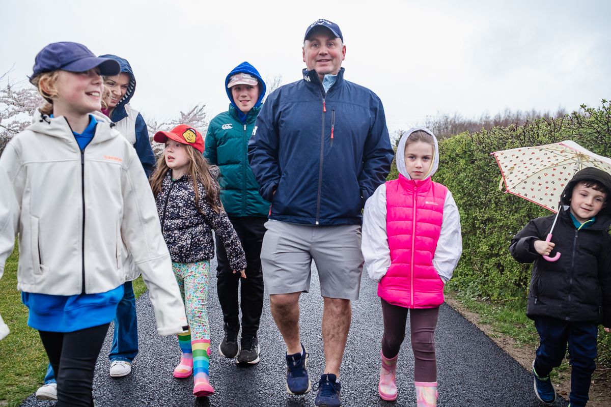 Group of adults and children walking together on a road in light rain, dressed in casual outdoor clothing.