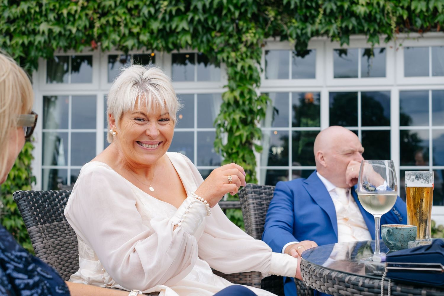 Smiling woman with short blonde hair enjoying a drink at an outdoor wedding reception venue.