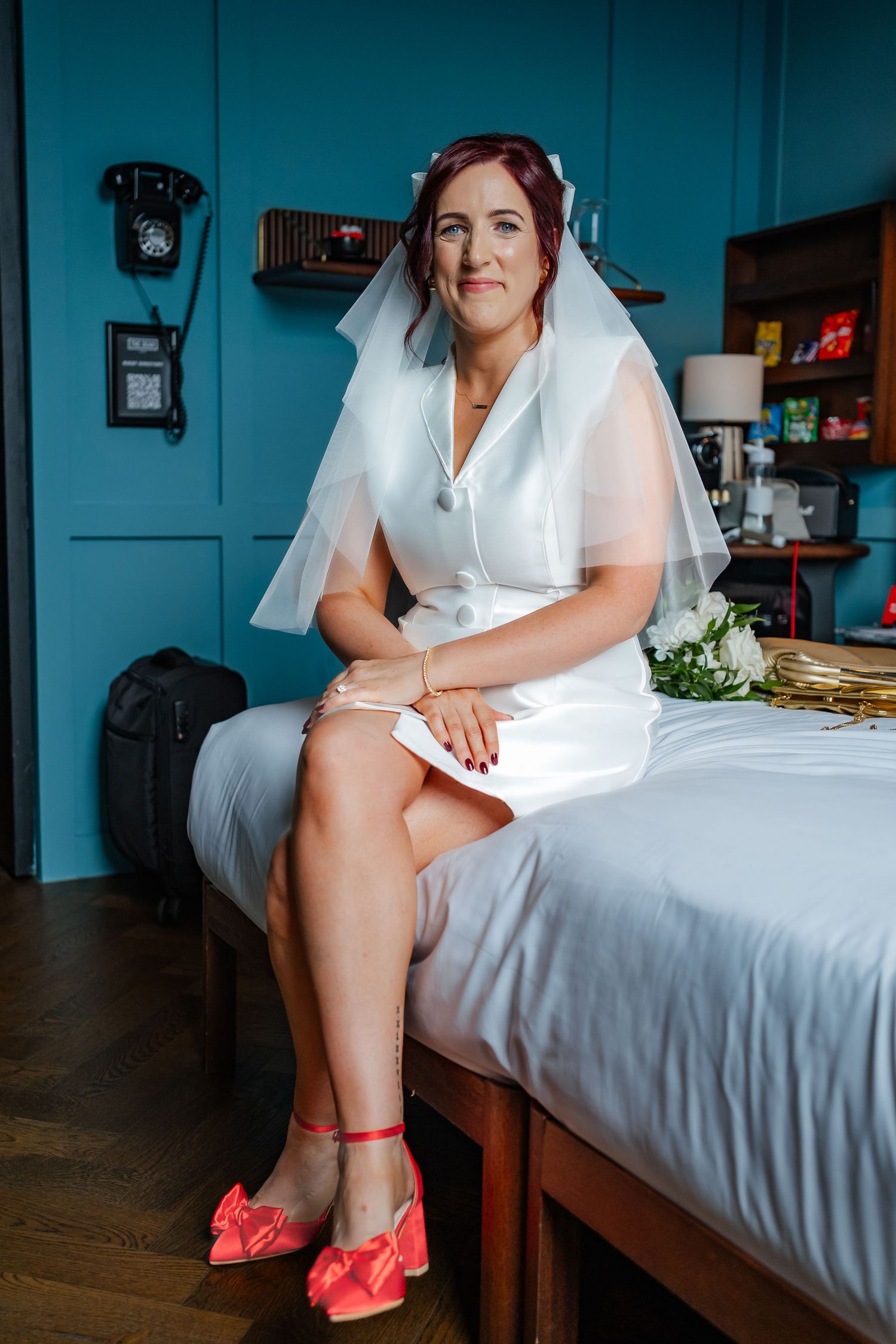 A bridal preparation scene showing bright coral pink wedding shoes on a bed.