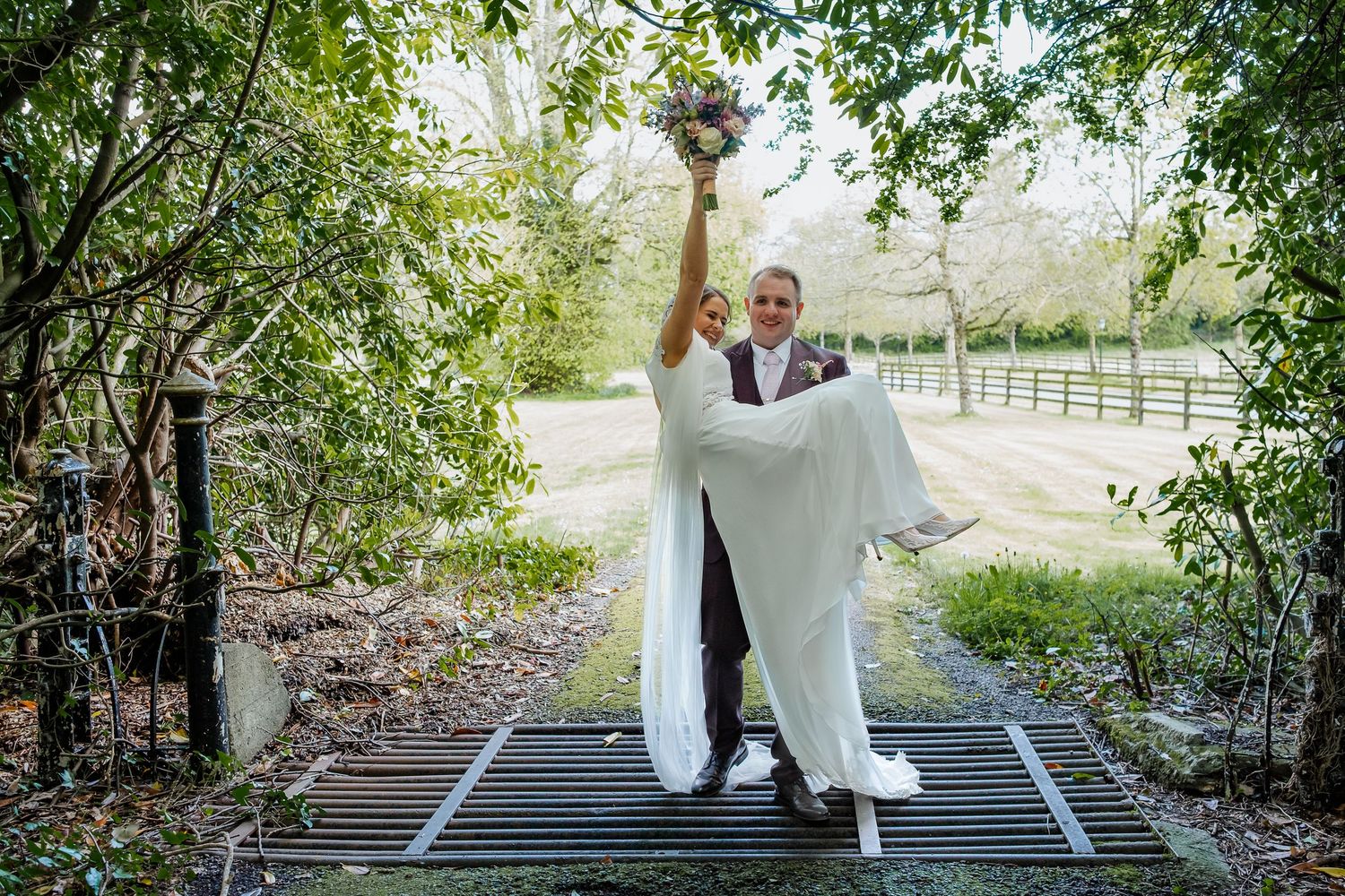 Wedding couple takes romantic outdoor portraits along a tree-lined path at a scenic countryside venue.
