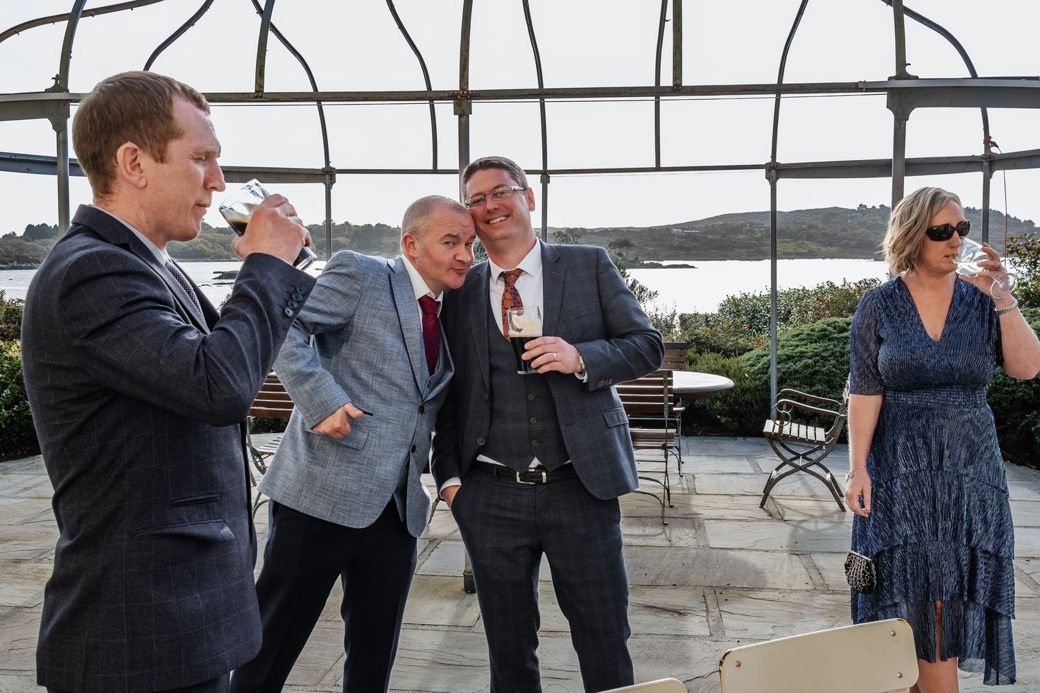 Guests in formal attire toast drinks on an outdoor terrace at a wedding reception.