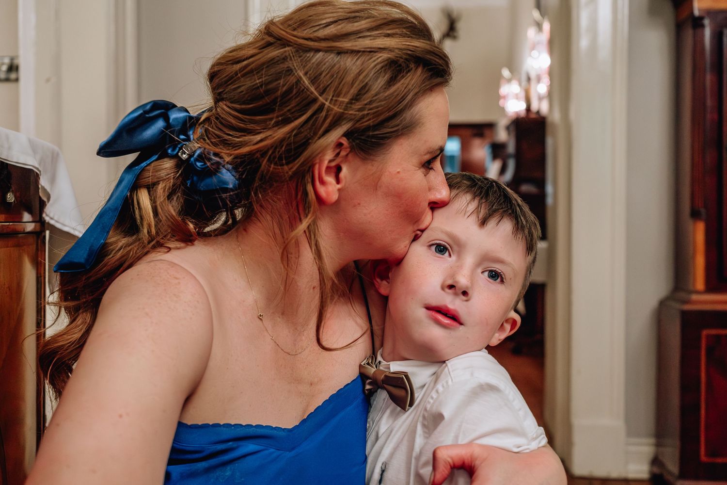Woman in blue dress tenderly kissing a young boy on the cheek at a wedding venue.