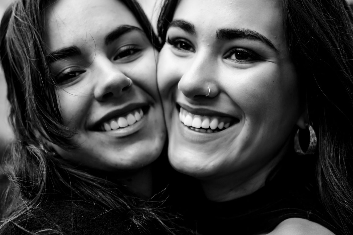 Two young women smiling and posing cheek to cheek in a black and white portrait photo.