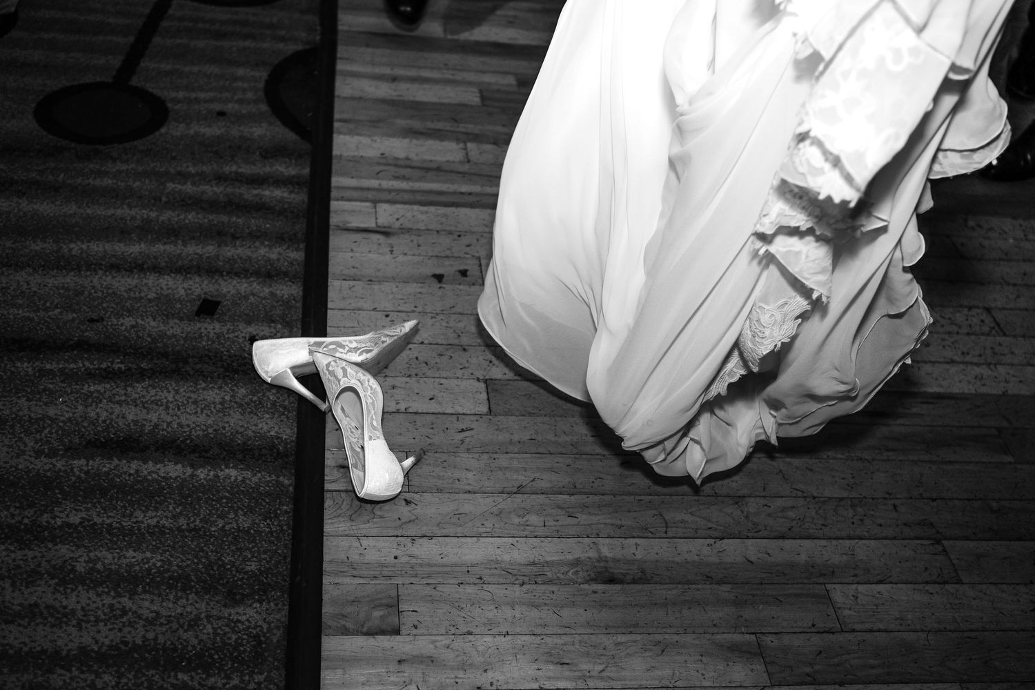 Black and white photo of ballet dancers rehearsing in a dance studio with hardwood flooring.