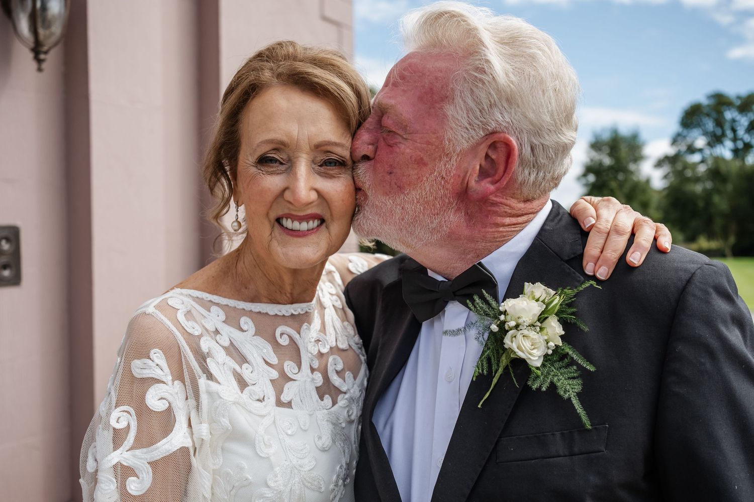 A tender moment between a couple in formal wedding attire outdoors.
