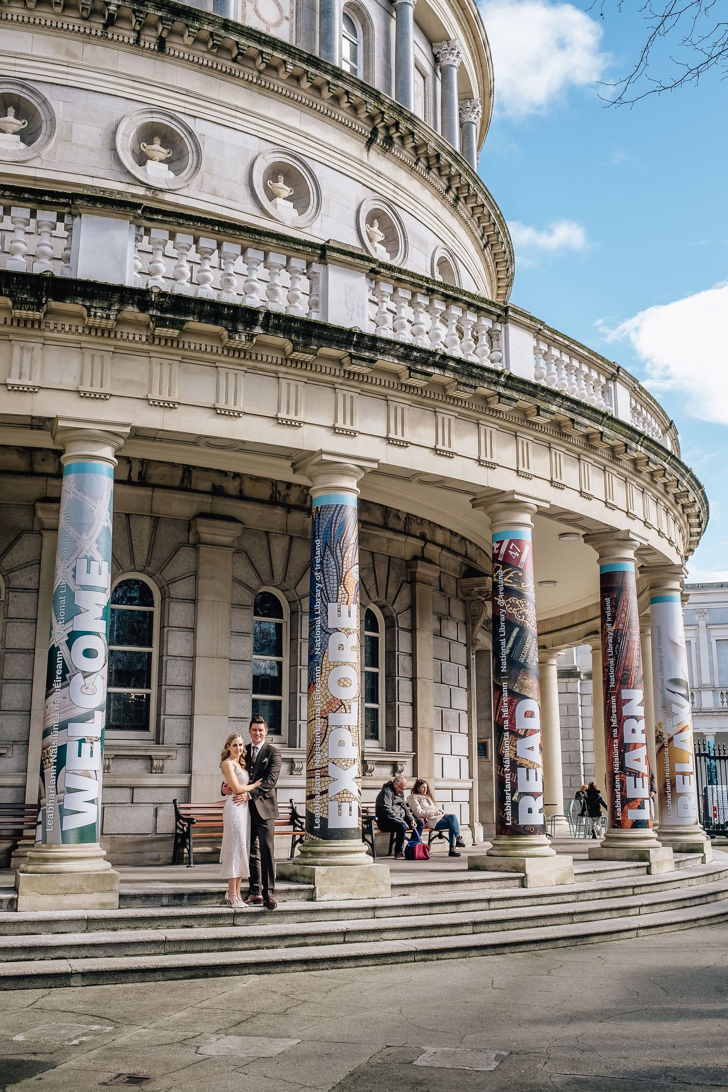 Couple poses on steps of historic building with classical columns and architectural details.