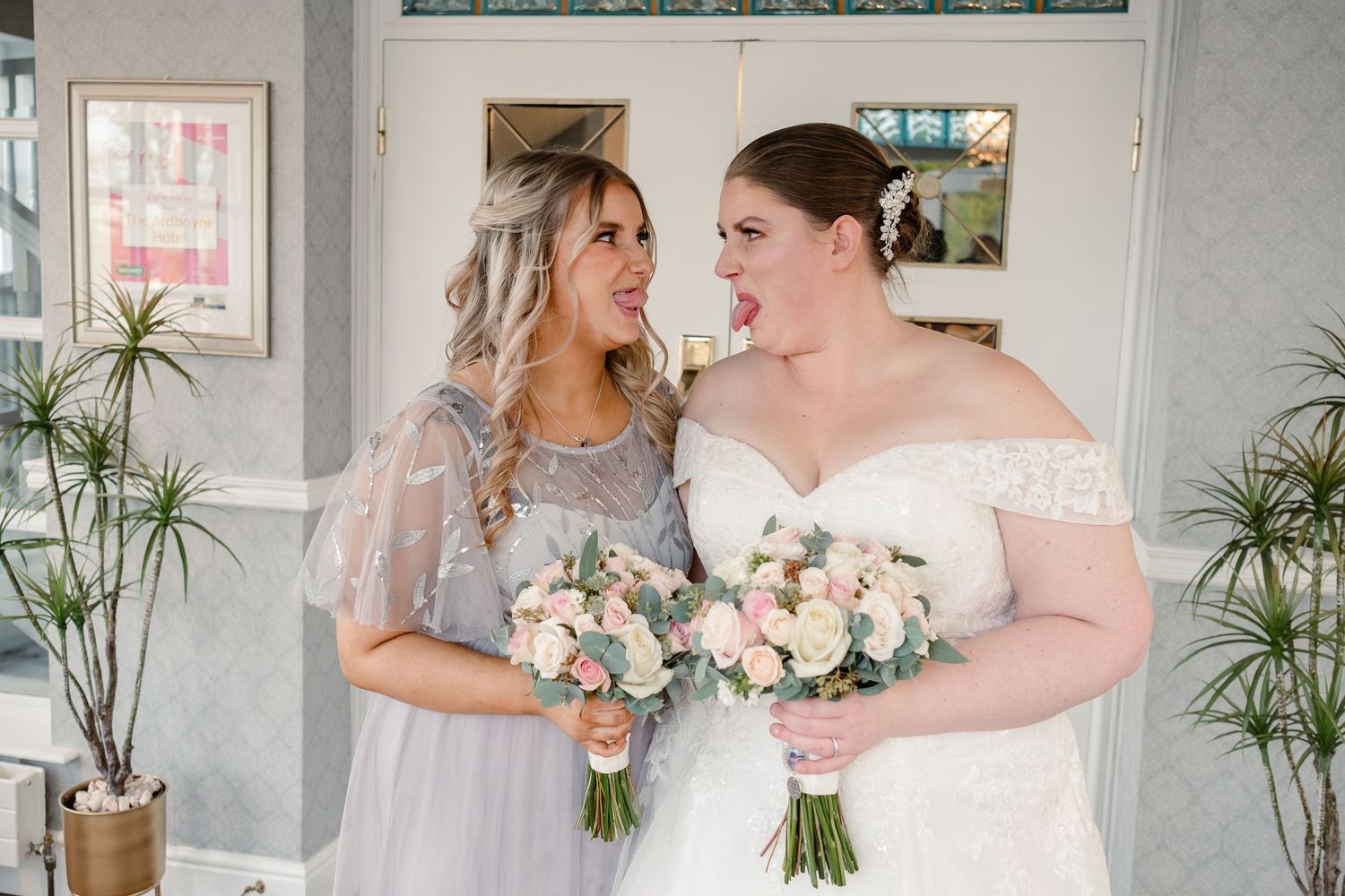 Two people holding matching pink and white bouquets in an indoor setting.