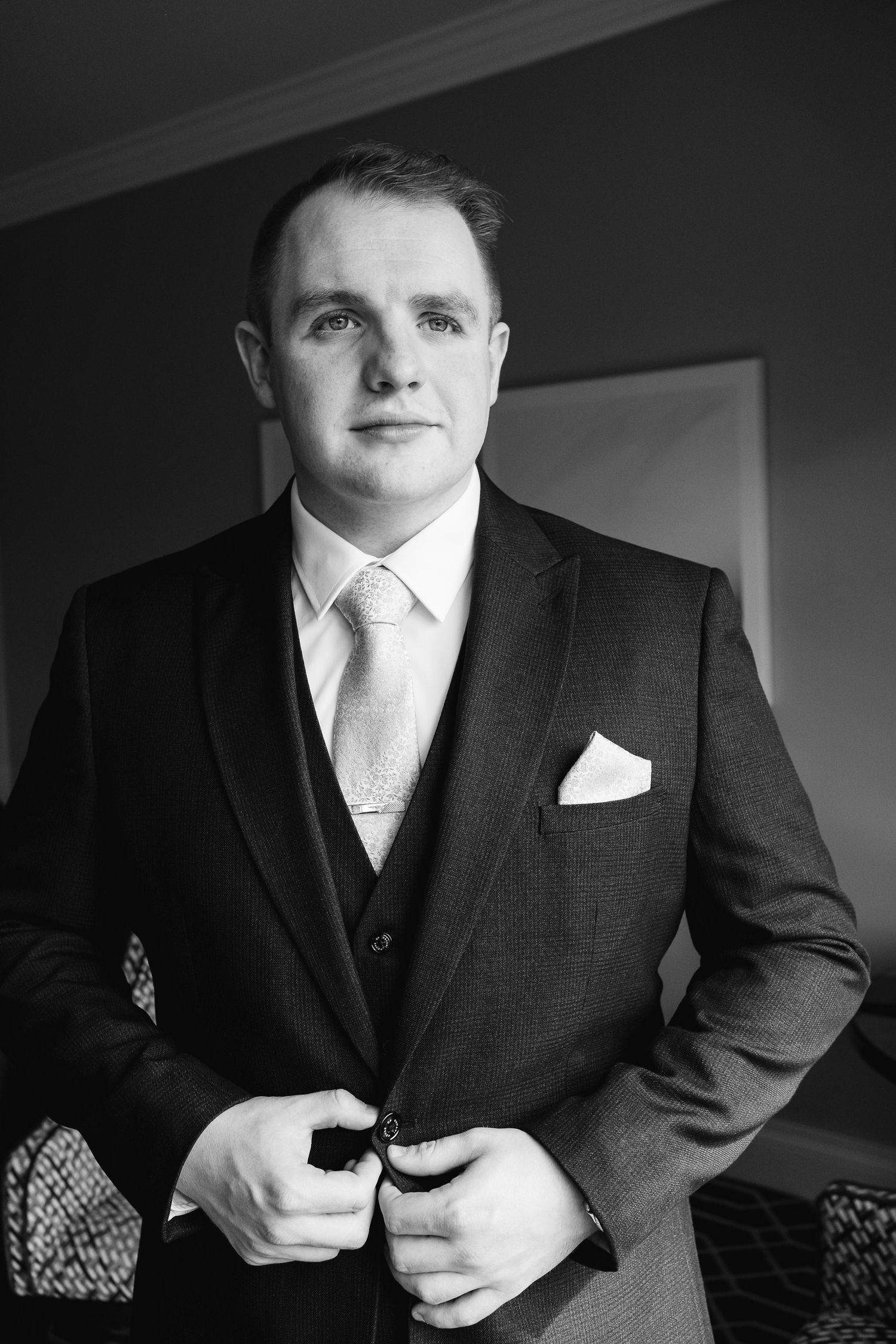 Black and white portraits of groom adjusting formal wear before wedding ceremony.