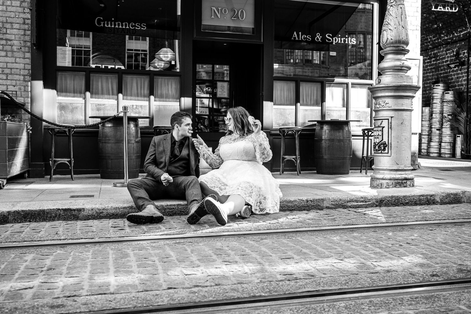Black and white street photography of couple sitting on cobblestone street.