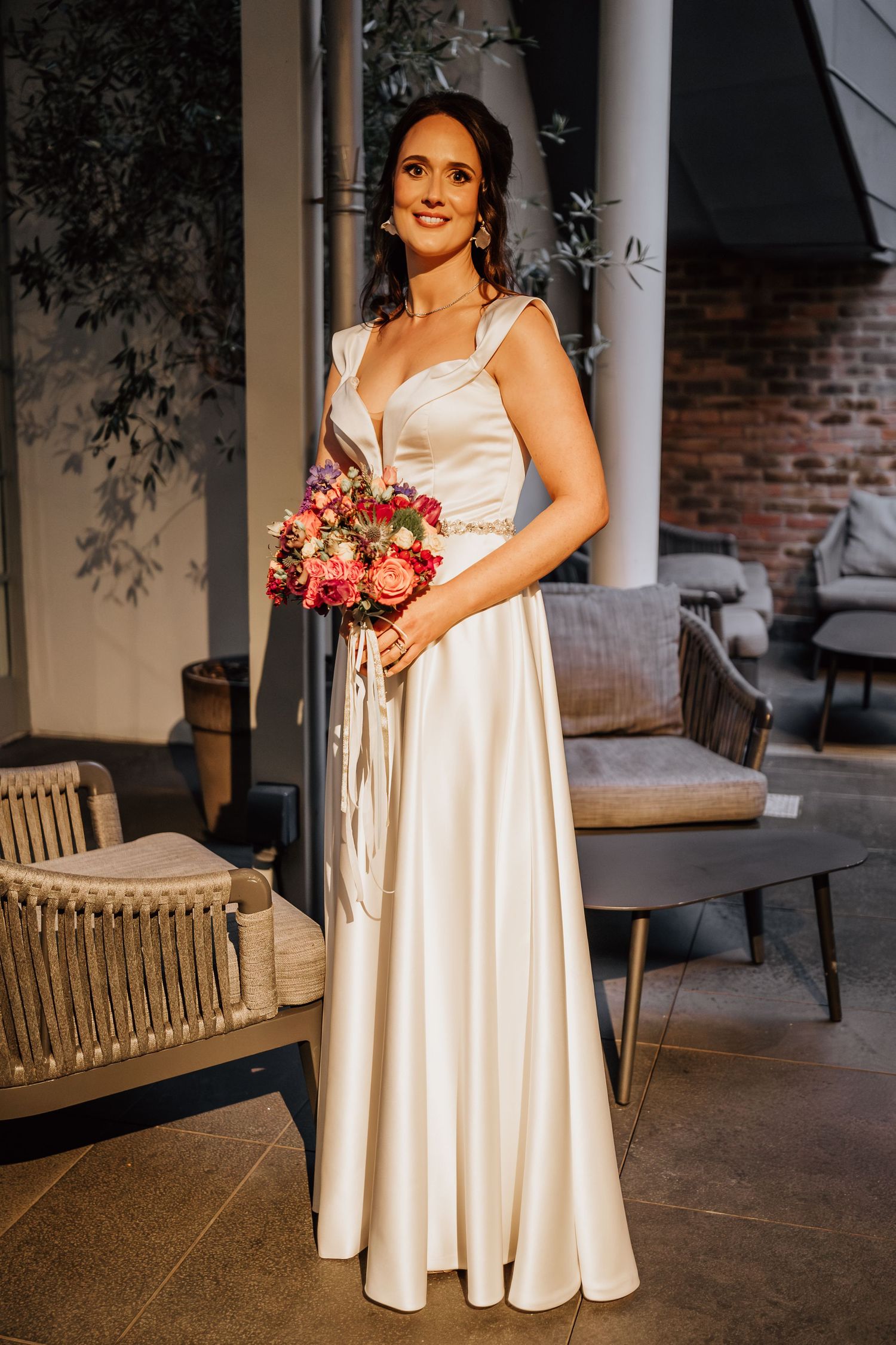 A bride in a classic white gown holds a vibrant pink bouquet while posing on an elegant porch.