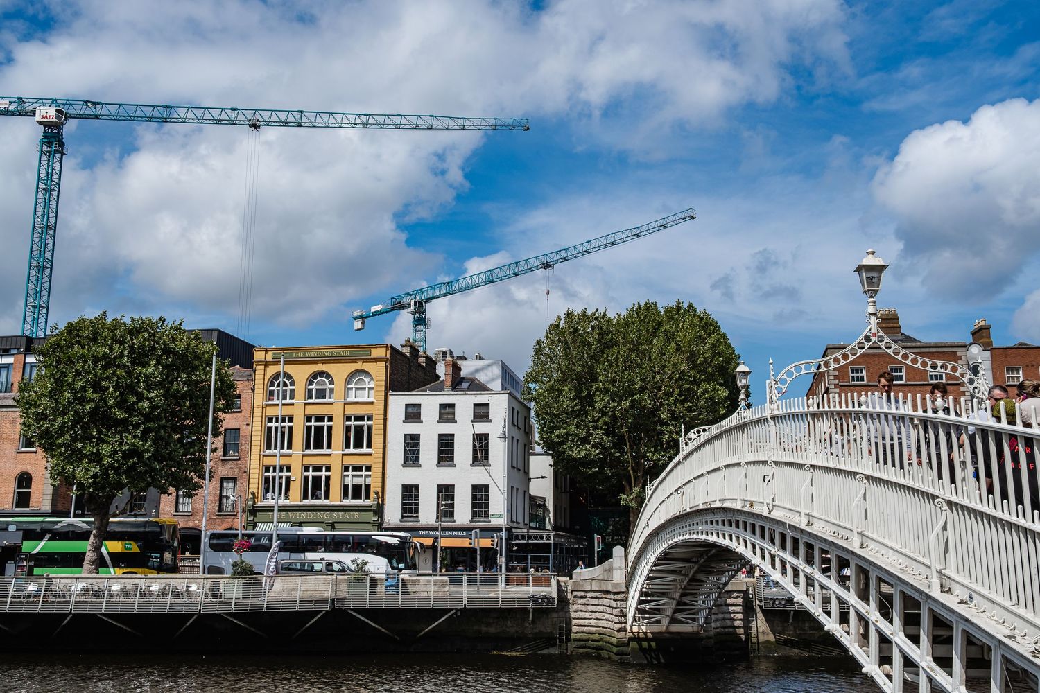 Historic Ha'penny Bridge spans the River Liffey in Dublin with white cast iron railings against blue cloudy sky.