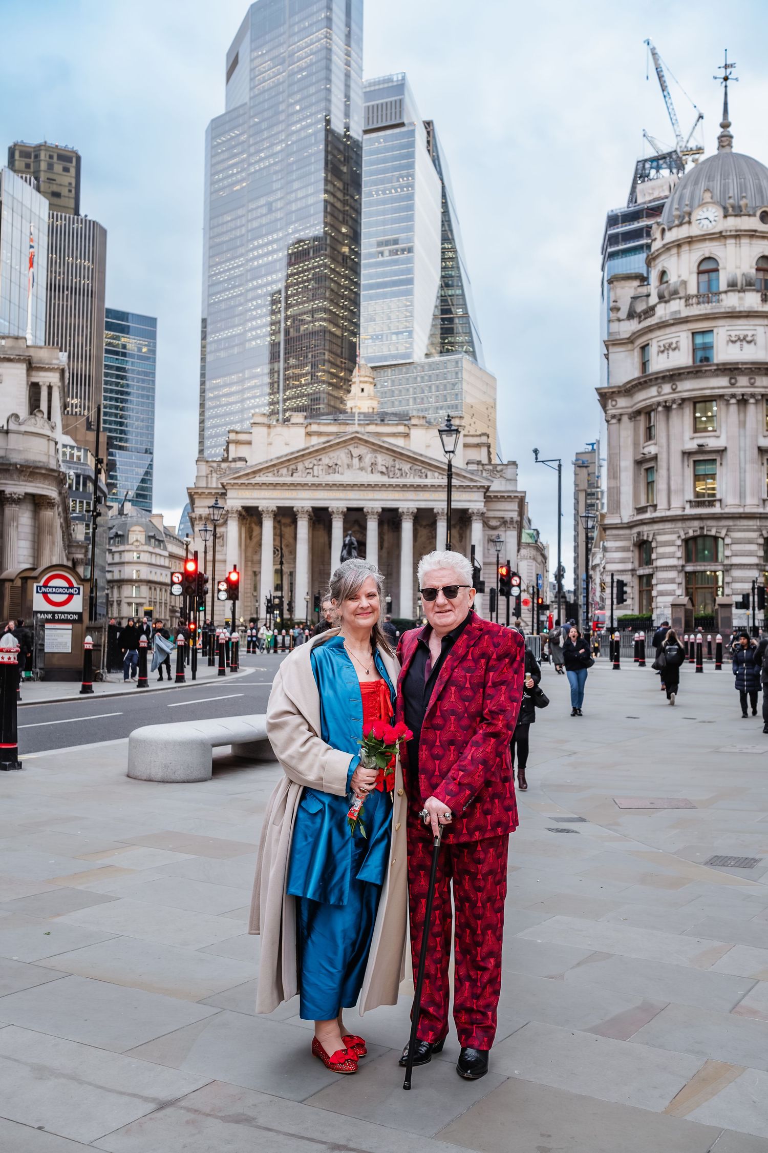 Couple posing in front of London's Royal Exchange with modern skyscrapers in background.