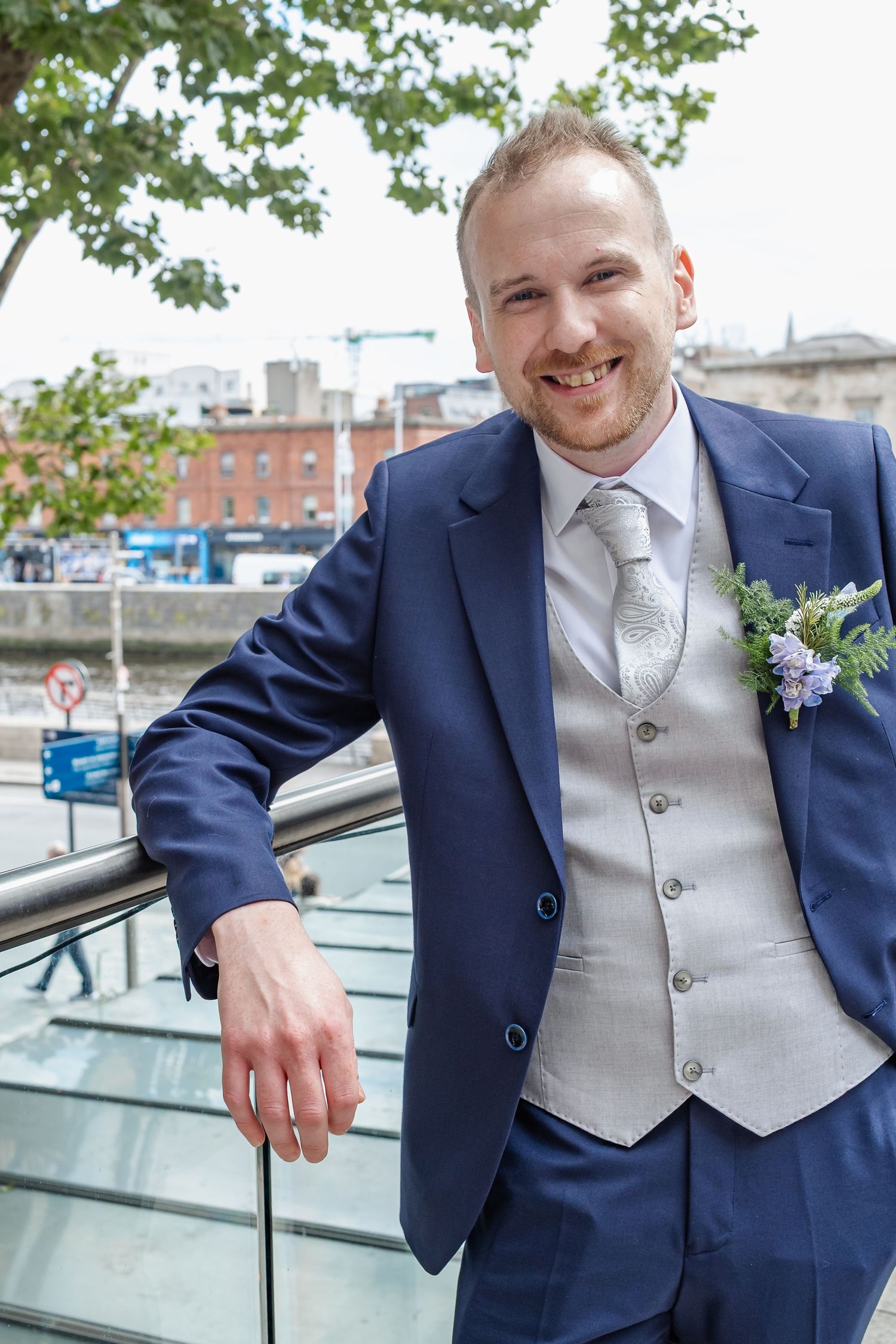 A series of four shots showing a groom in a navy suit and silver vest posing outdoors with a happy expression.