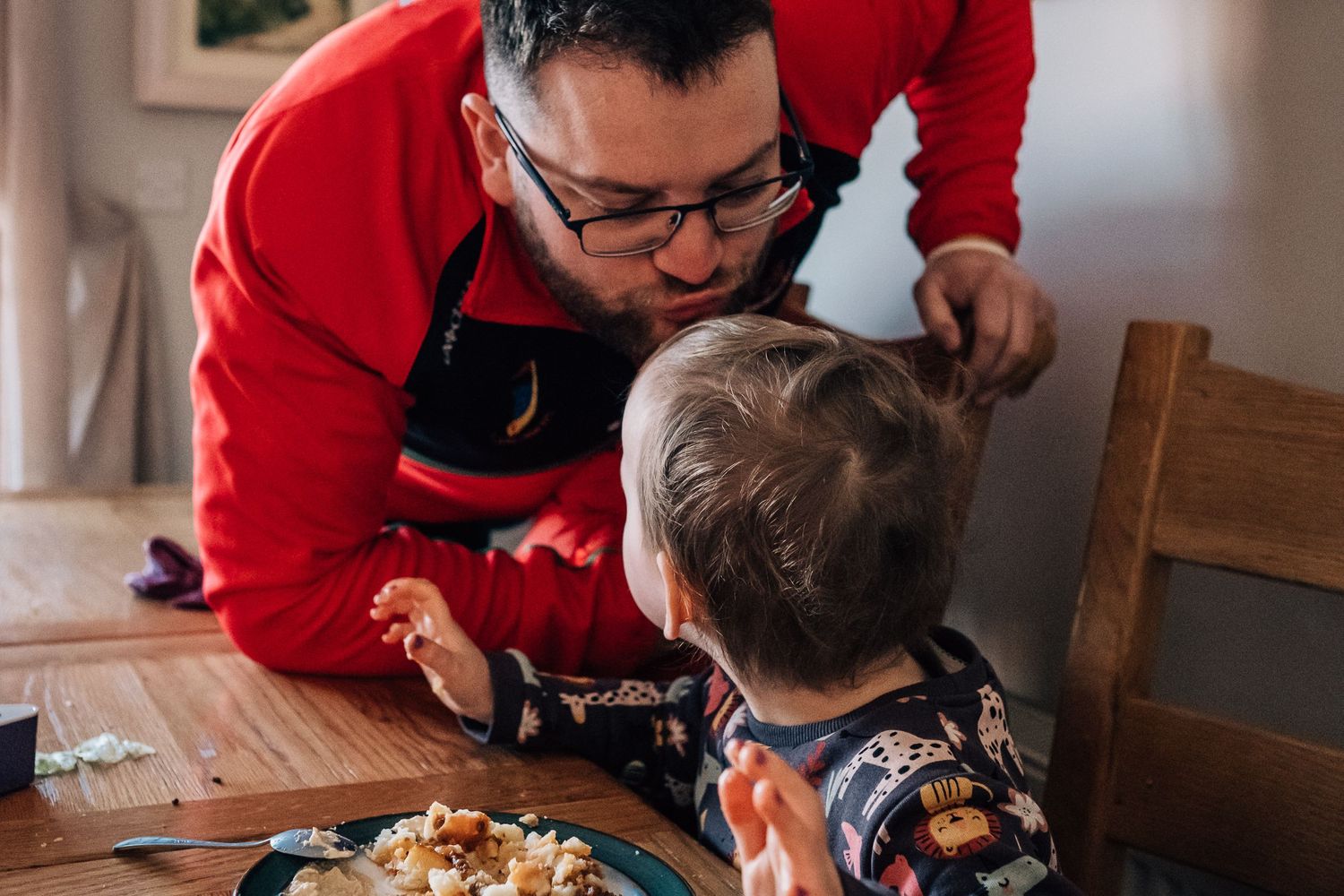 Two people examining food together at wooden dining table.