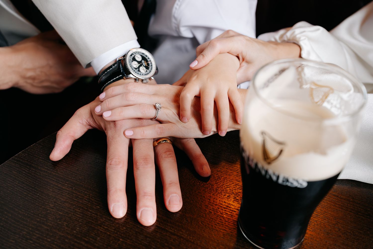 Newlywed couple displaying wedding rings on a wooden table beside a Guinness pint glass.