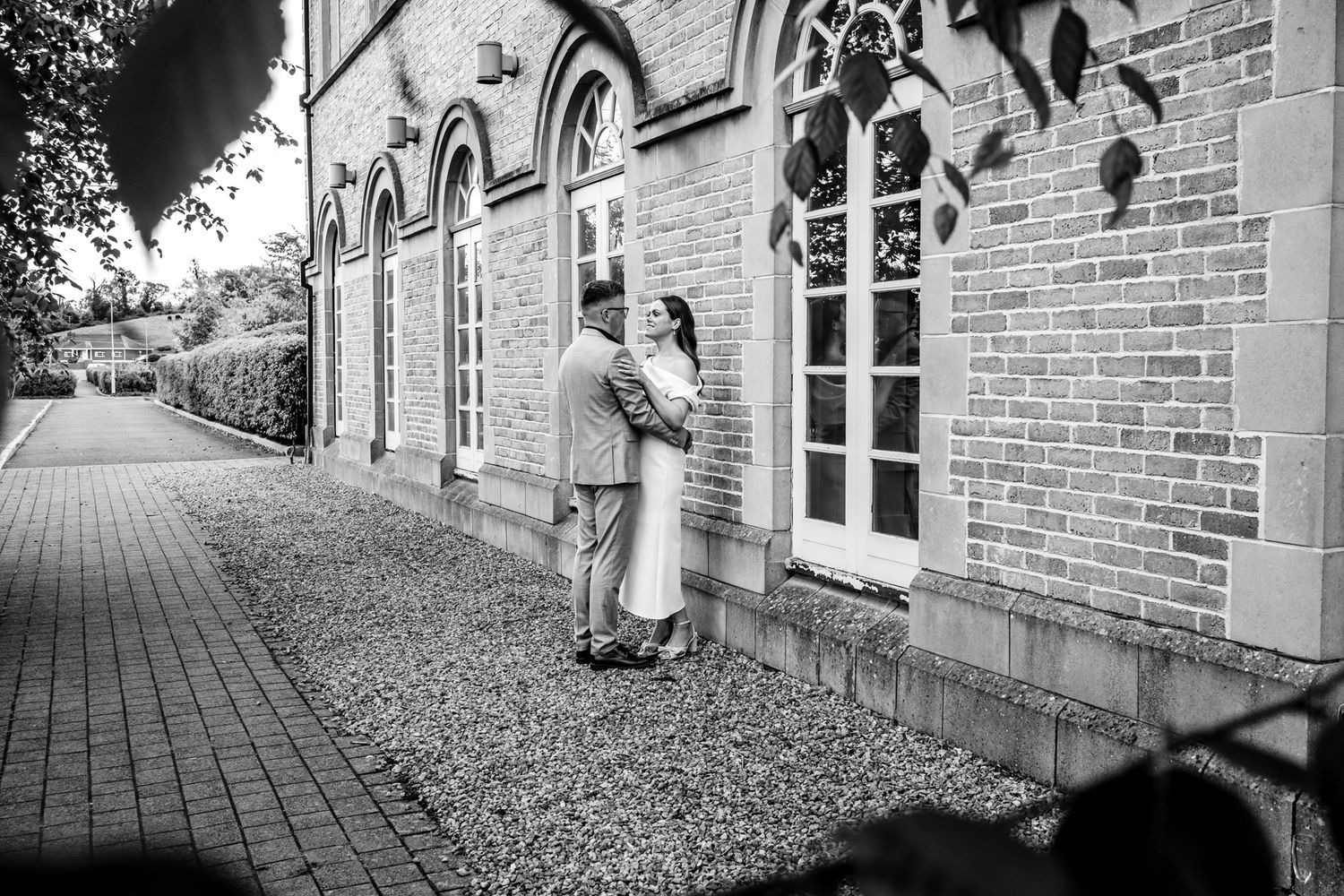 Black and white romantic moment against historic brick building with arched windows.