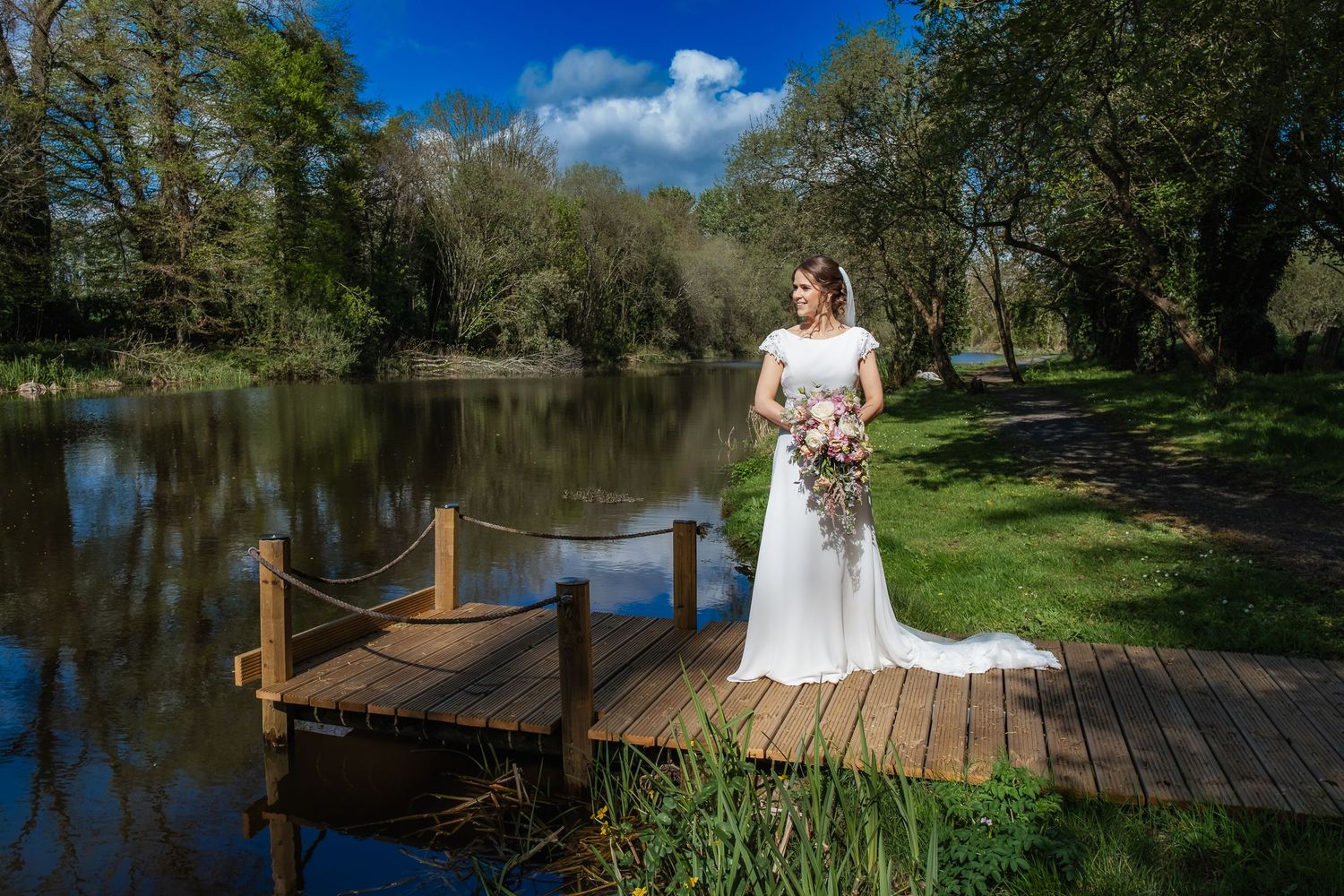Outdoor bridal portraits taken on wooden dock overlooking serene lake on sunny day.