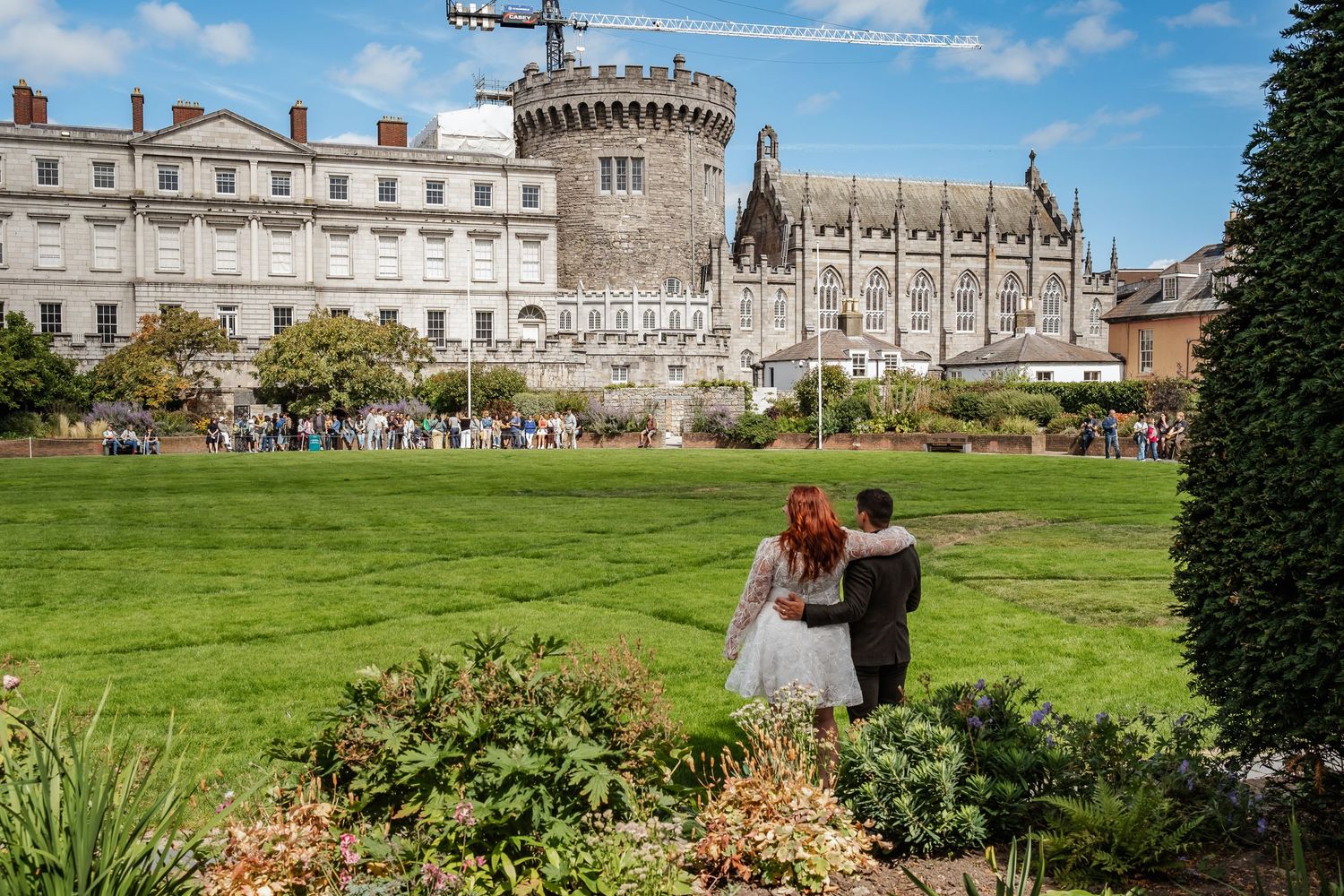 A couple walks across manicured grounds with a stunning medieval castle in the background.