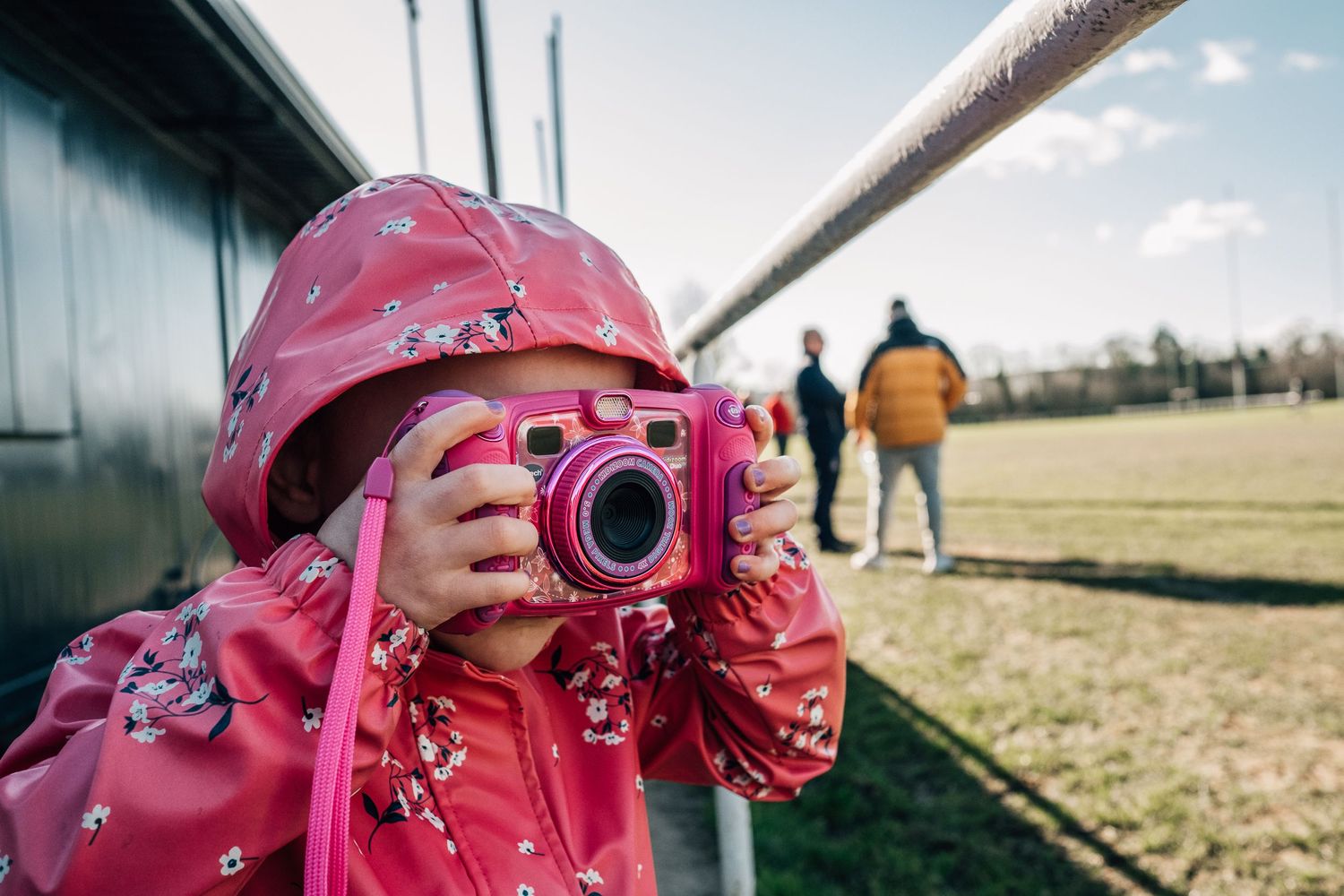 A small photographer in a pink raincoat taking pictures with a camera outdoors.