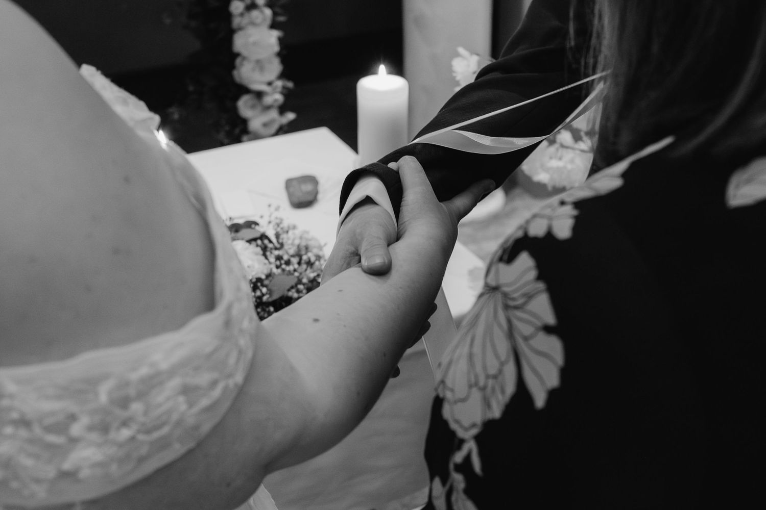 Black and white detail shot of hands holding a wedding unity candle during ceremony.