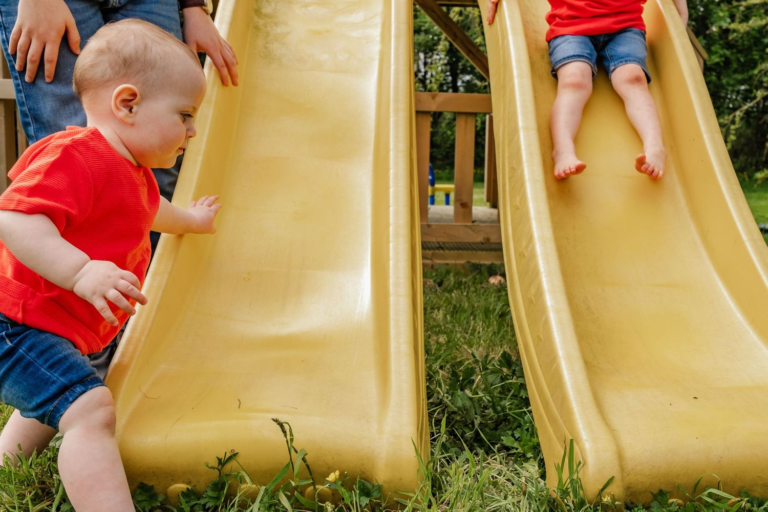 Children playing on yellow playground slides in a backyard.