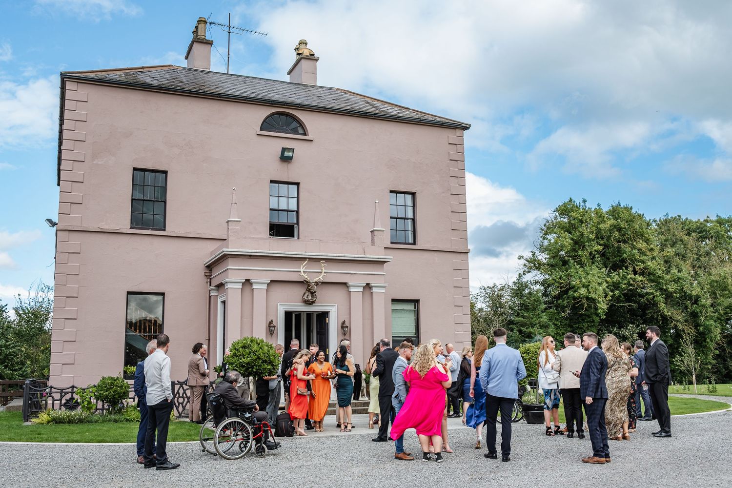 Wedding guests gathering outside a pink Georgian-style house for celebration photos.