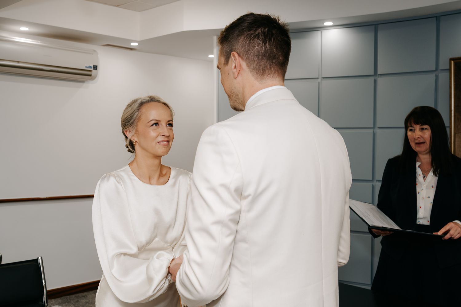 Couple exchanging vows at a civil wedding ceremony with an officiant holding a book in the background.