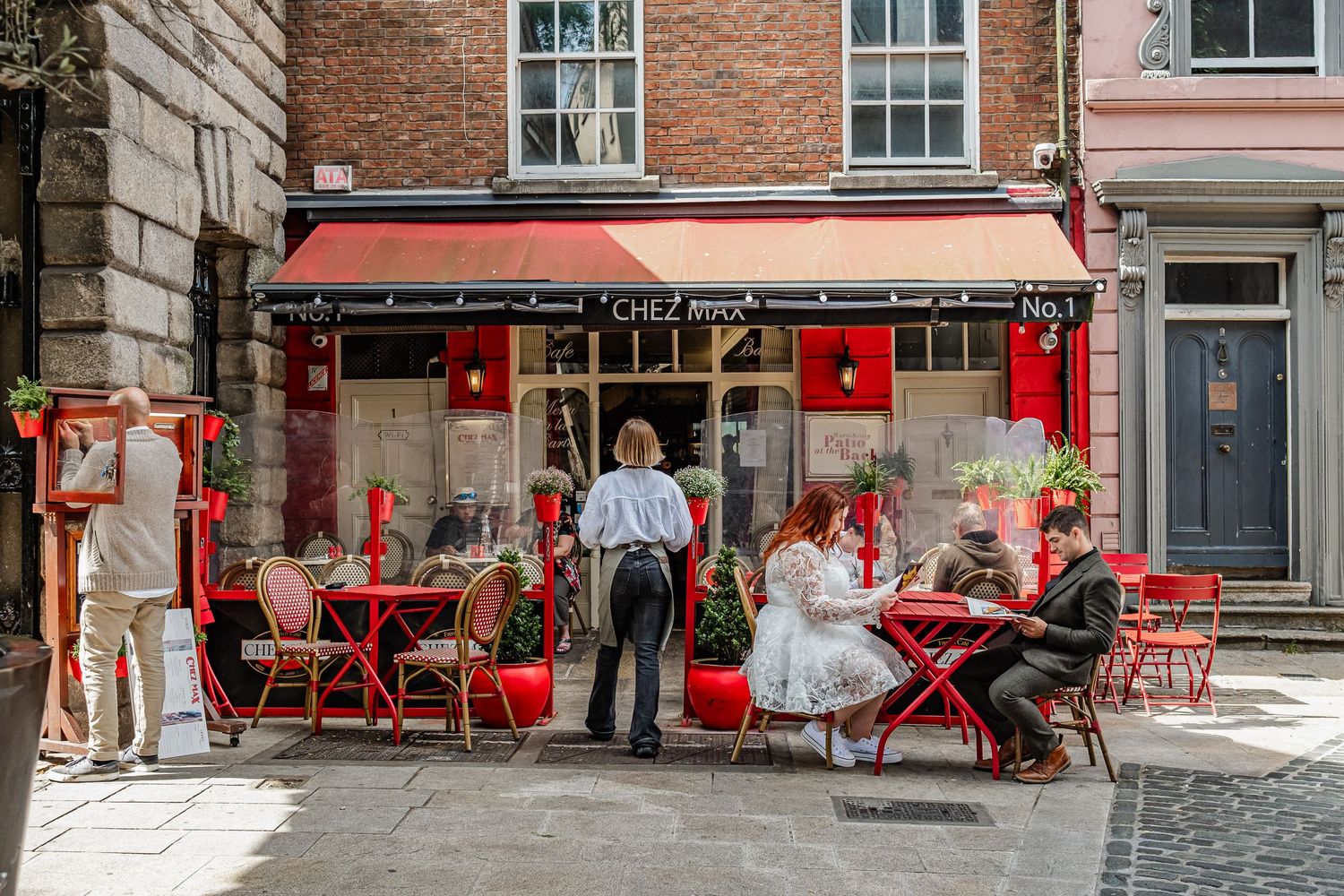 A quaint street cafe with red decor and outdoor seating showing diners enjoying their meals.