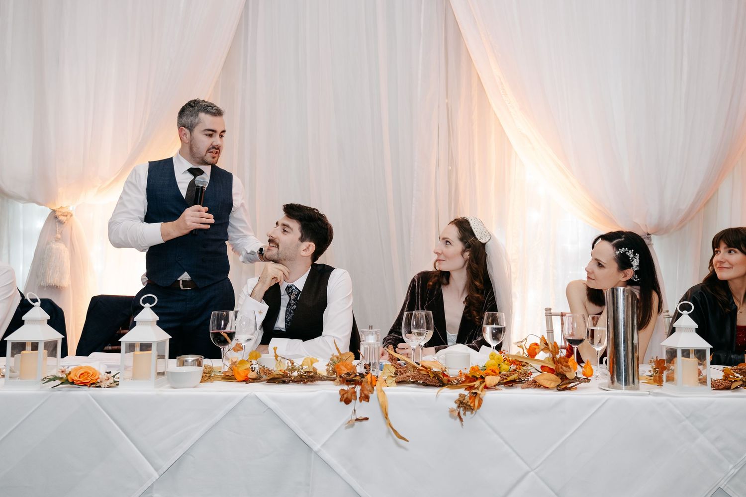 Wedding reception guests seated at elegant tables with warm lighting and autumn decor.