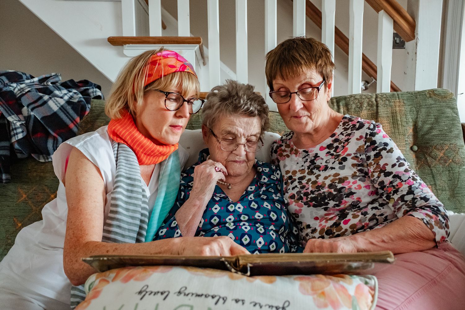 Three people look at an old photo album together while sitting on a couch.