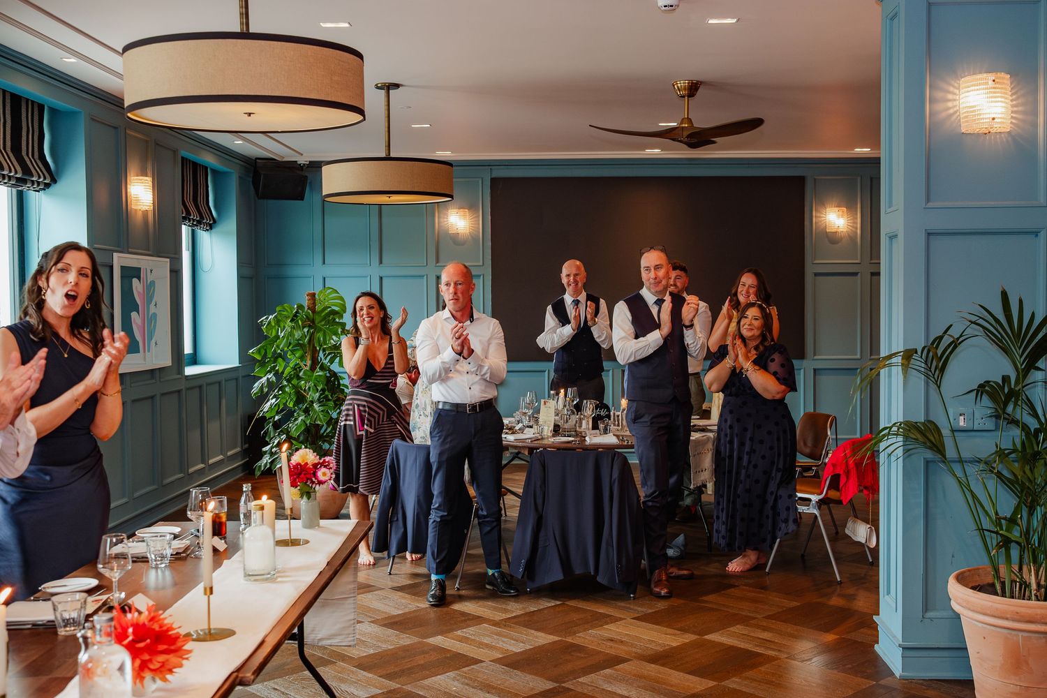 A panoramic view of a wedding reception celebration in a restaurant with teal blue walls and wooden floors.