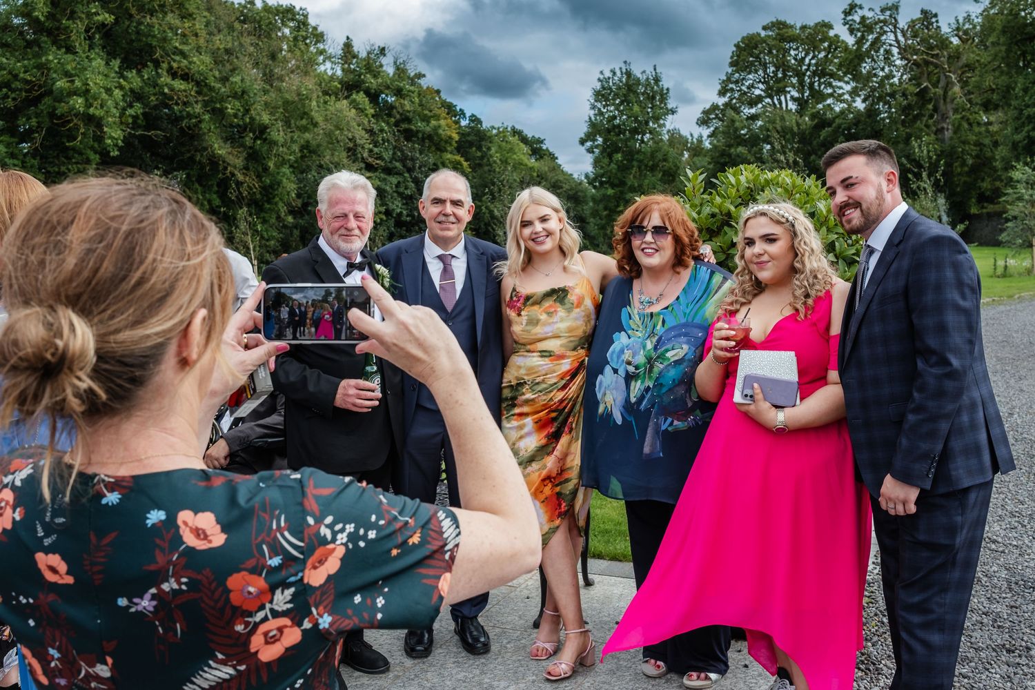 Wedding photographer capturing group photos of guests outdoors on a cloudy day.