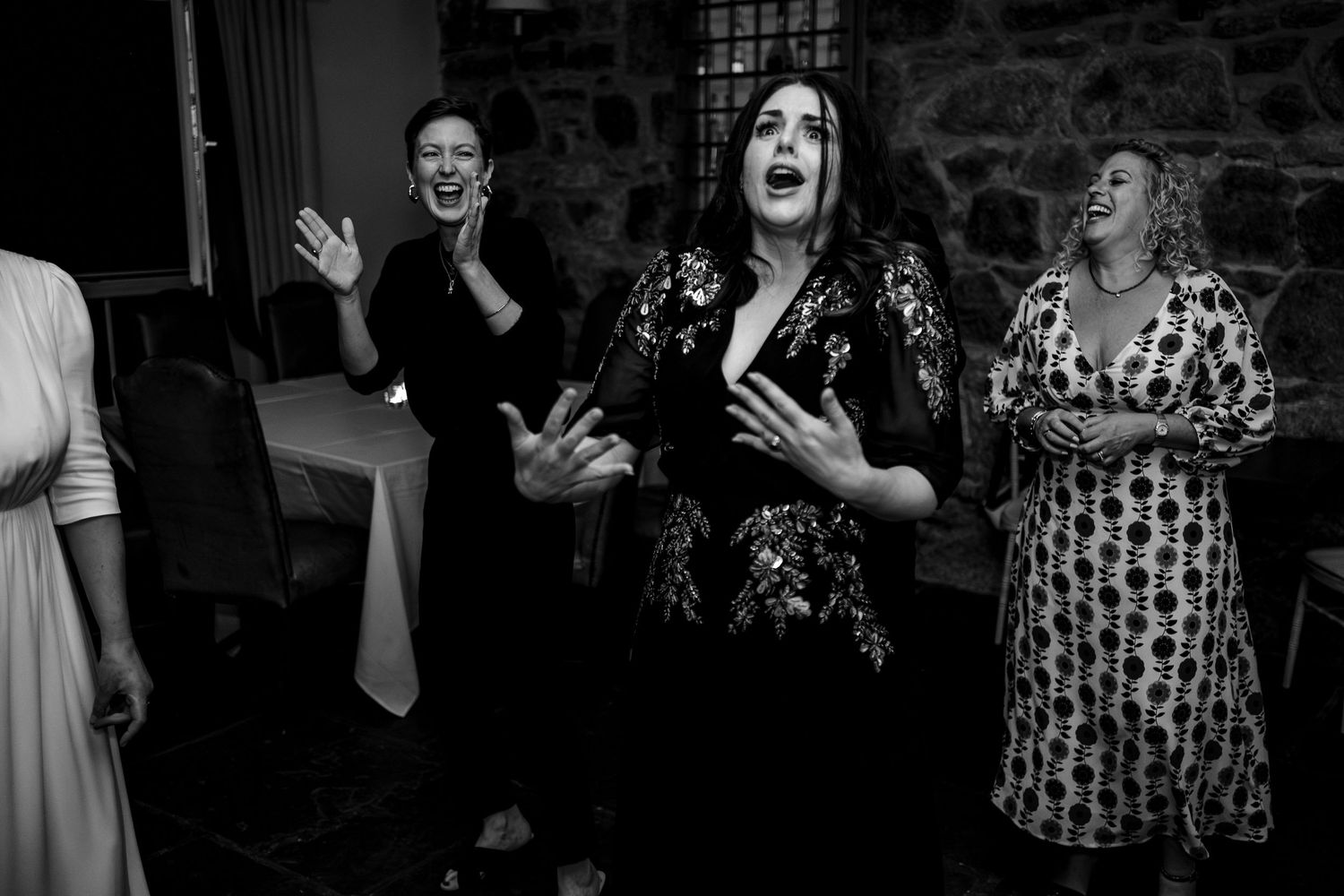 Black and white photo of three women singing and celebrating at a wedding reception.