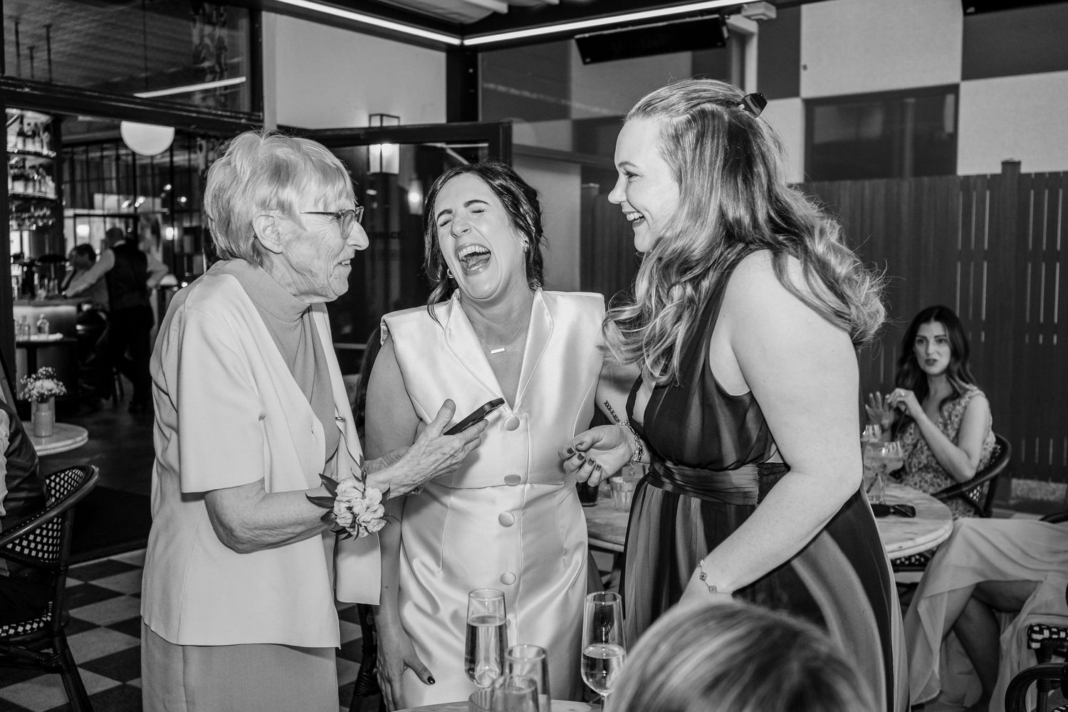Three women laughing and socializing at an indoor event in black and white photo.